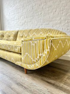 a yellow couch sitting on top of a hard wood floor next to a white brick wall