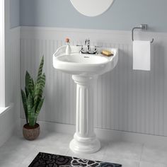 a white pedestal sink sitting in a bathroom next to a mirror and toilet paper roll