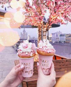 two people holding up ice cream cones with pink frosting and sprinkles