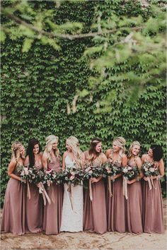 a group of women standing next to each other in front of a wall covered with greenery