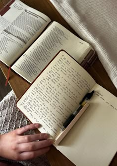 an open book with writing on it and a person holding a pen next to it