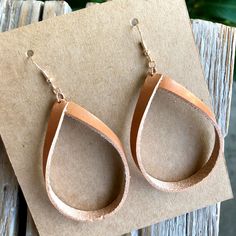 a pair of leather tear earrings sitting on top of a piece of cardboard next to a plant