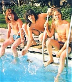 three young men are sitting on the edge of a swimming pool and posing for a photo