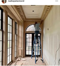 a man on a ladder painting the ceiling in an empty room with windows and doors