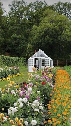 a garden filled with lots of flowers next to a white house in the middle of trees