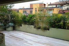 a wooden deck with planters and trees in the back yard, surrounded by tall buildings