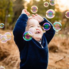 a toddler playing with soap bubbles in the air on a fall day at the park