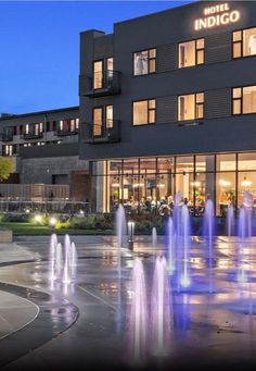 the hotel indigo is lit up at night with water fountains in front and people walking around