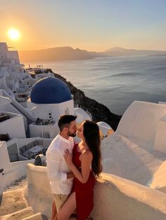 a man and woman are sitting on the steps next to the ocean in front of some buildings