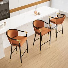 two orange chairs sitting next to each other on top of a hard wood floor in front of a white counter