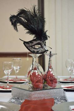 a table topped with two vases filled with red flowers and black feathered masks