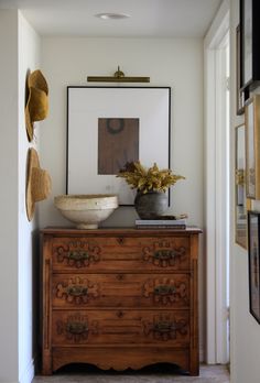 a wooden dresser sitting in the middle of a hallway next to a wall with pictures on it