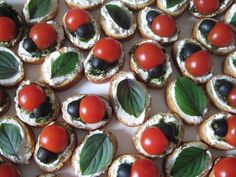 small appetizers with tomatoes, olives and spinach leaves on them sitting on a white platter