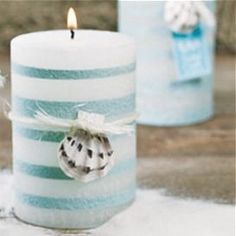 two blue and white striped candles are on the ground with snow around them, one candle has a small ornament hanging from it