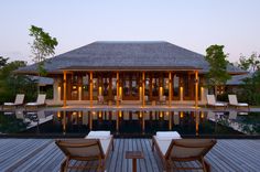 two chairs sitting on top of a wooden deck next to a swimming pool at dusk