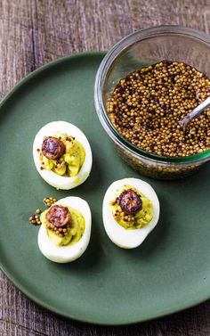 three deviled eggs on a green plate with mustard and seasoning in a bowl