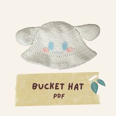 a crocheted white hat with blue eyes and pink nose is next to a piece of paper that says bucket hat