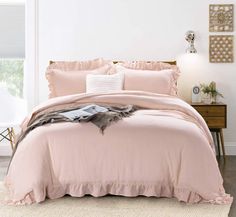 a bed with pink comforter and pillows in a white room next to a window