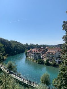 people are walking on a bridge over a river with houses in the background and trees lining both sides