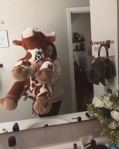 a woman holding a large stuffed giraffe in front of a bathroom vanity mirror