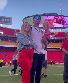 a man and woman are standing on the field with a baby in their arms at a football game