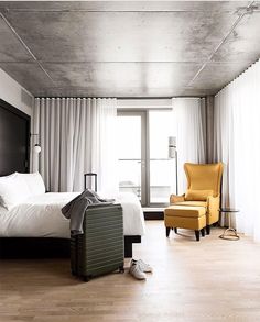 a bedroom with a bed, chair, and window in the room that has white curtains