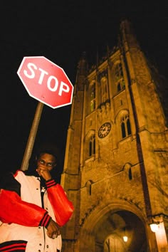 a man standing next to a stop sign in front of a tall building at night