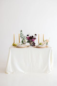 a table topped with two plates covered in flowers and candles next to a vase filled with greenery