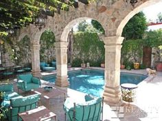 an outdoor swimming pool surrounded by stone pillars and arches with seating around the pool area