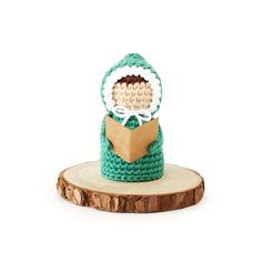 a crocheted doll is sitting on top of a piece of wood and wearing a green sweater