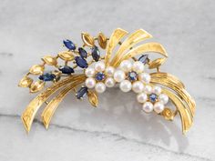 A stunning vintage piece, full of color, texture and overall visual impact! Set with round and marquise cut sapphires and creamy pearls, this floral themed brooch has hand-etched ribbons of gold, finished with a perfect patina, absolutely gorgeous! Love this piece, but want to make it more versatile? We here at Market Square Jewelers, along with our master metalsmiths can convert this fantastic brooch into a necklace or pendant for an additional fee. Please contact us for more information! Metal Vintage Pearl Brooch, Sapphire And Pearl, Marquise Sapphire, Market Square, Wedding Brooch, Cameo Ring, Pearl Brooch, Natural Pearl, Flower Wedding