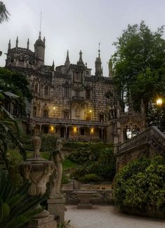 an old castle with statues in front of it at night time, surrounded by greenery and trees