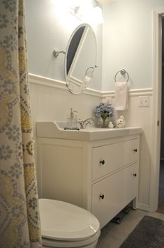 a white toilet sitting next to a bathroom sink under a mirror and a shower curtain