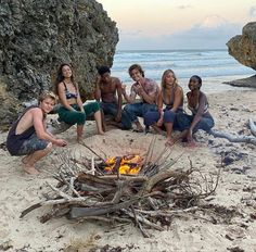 five people sitting around a campfire on the beach