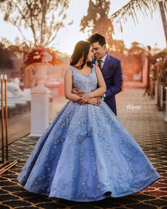 a man and woman standing next to each other in front of a fountain wearing blue dresses