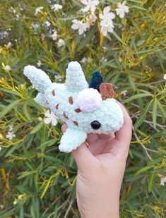 a hand holding a small crocheted animal in front of some flowers