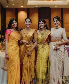 three women standing next to each other in yellow sari and red blouses, posing for the camera