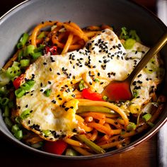 a bowl filled with noodles, vegetables and tofu on top of a wooden table