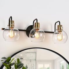 a bathroom vanity light with three clear globes on it's sides and a round mirror over the sink