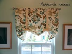 a kitchen window with a valance hanging over it's windowsill and two framed pictures on the wall