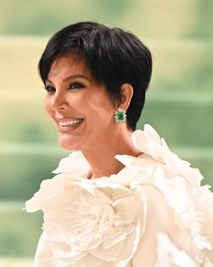 a woman in a white dress smiles at the camera while wearing green and white earrings