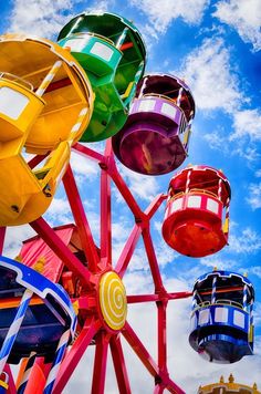 the ferris wheel is brightly colored and stands in front of a blue sky with clouds