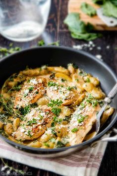 a skillet filled with pasta and chicken covered in parmesan cheese on top of a wooden table