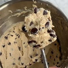 a person holding a spoon in a metal bowl filled with ice cream and chocolate chip cookies