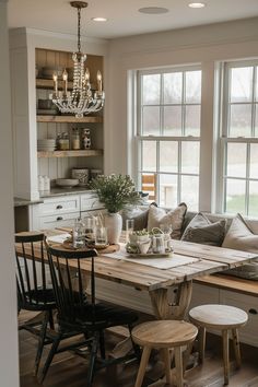 a dining room table with chairs and a bench in front of two large windows that are open to the kitchen