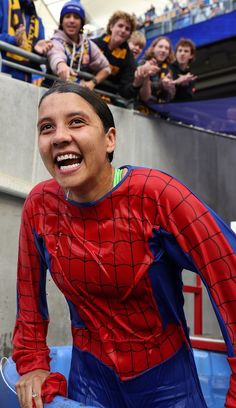 a man in a spider suit is smiling for the camera while people watch from behind him