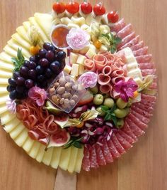 a platter filled with different types of meats, cheeses and fruit on a wooden table