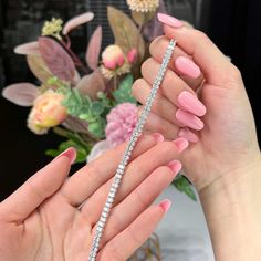 two hands holding a diamond bracelet in front of a vase with flowers and greenery