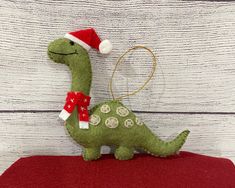 a stuffed toy dinosaur with a santa hat on it's head sitting on a red pillow