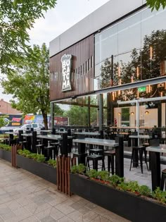 the outside of a restaurant with tables and chairs in front of glass walls that have plants growing on them